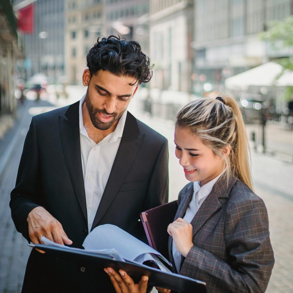 Young business professionals in formal attire reviewing documents outdoors, showcasing teamwork.