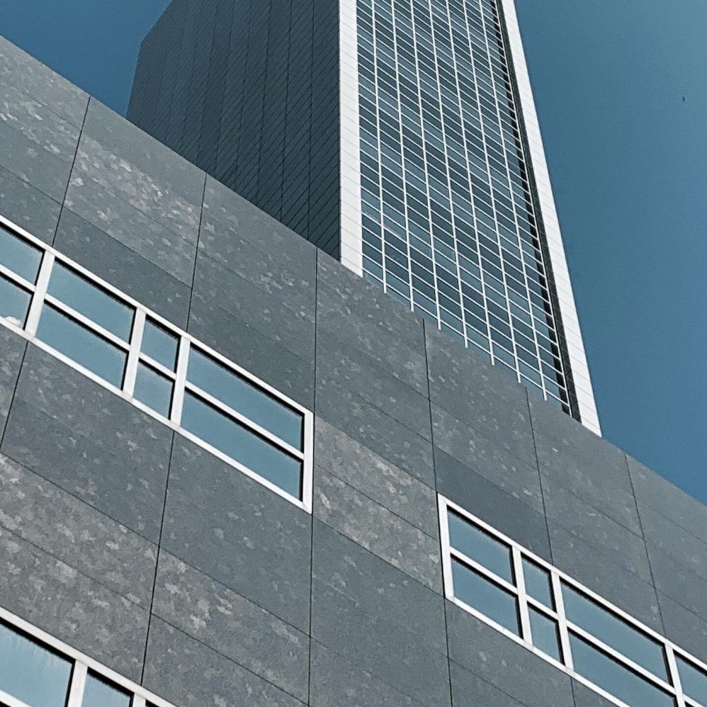 Low-angle view of a modern skyscraper in Amsterdam, showcasing sleek architecture against a clear blue sky.